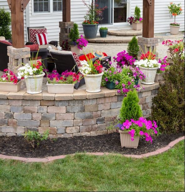 A backyard with a paver patio, stone steps, and stone block wall decorated with colorful flowers.