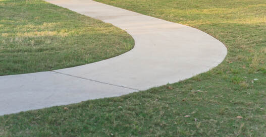 A curved poured concrete sidewalk surrounded by grass.